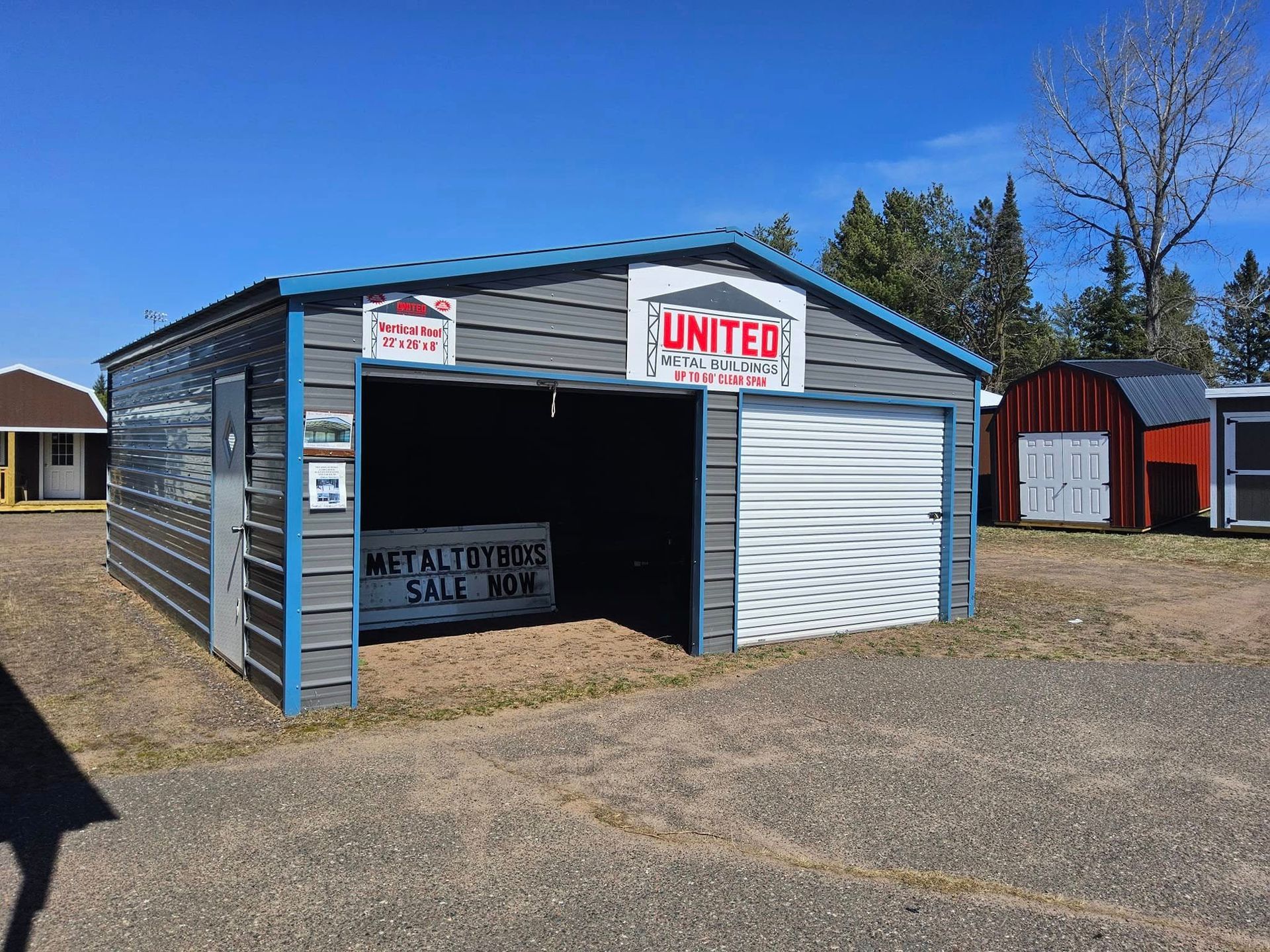 Small gray storage building with open garage door and UNITED signs on a gravel lot under a blue sky
