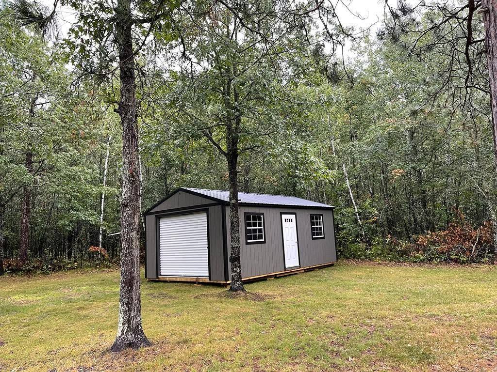 Small gray shed with white doors in a grassy wooded yard