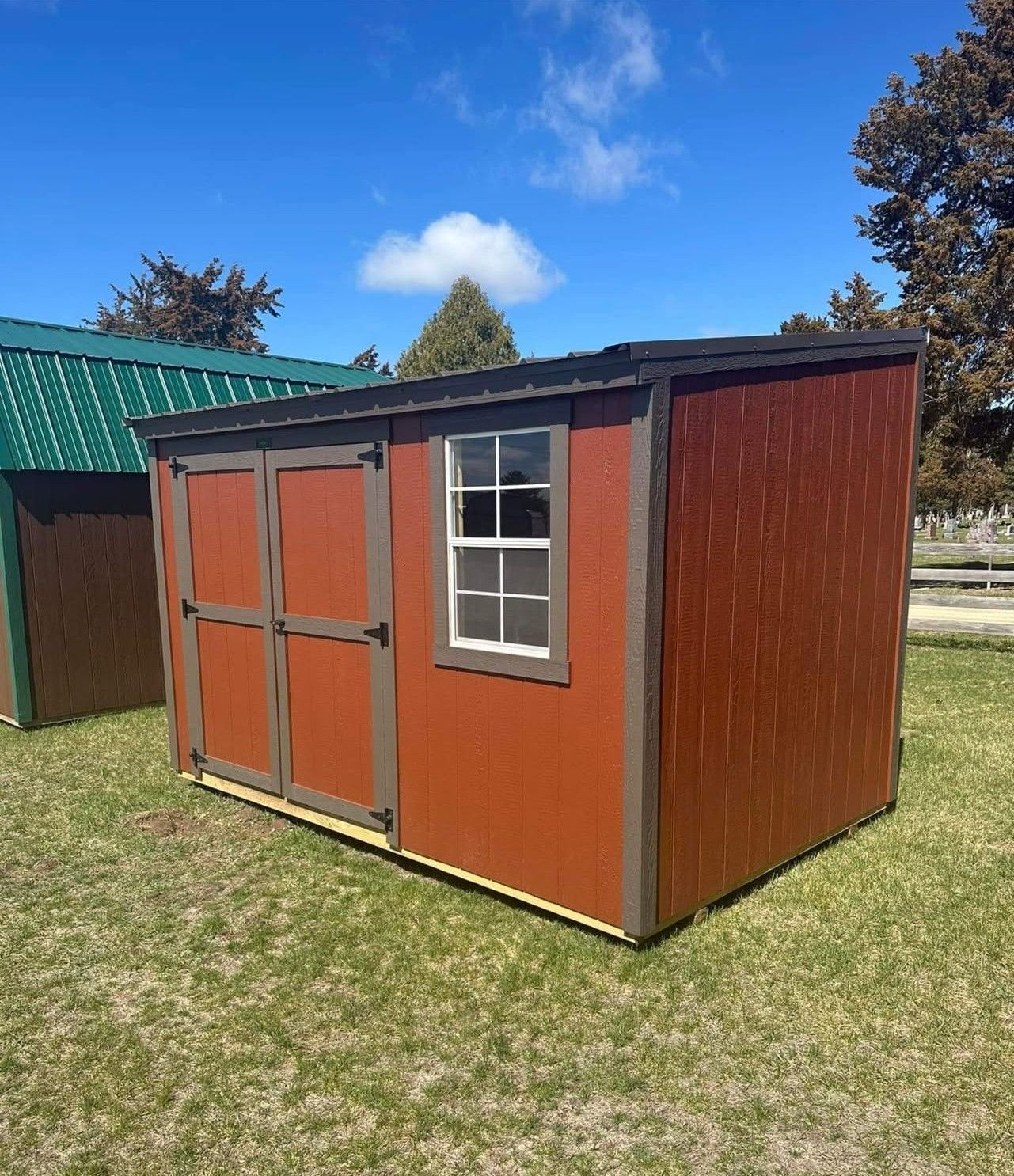 Small orange storage shed with a green roof and white-trimmed window on a grassy lawn.