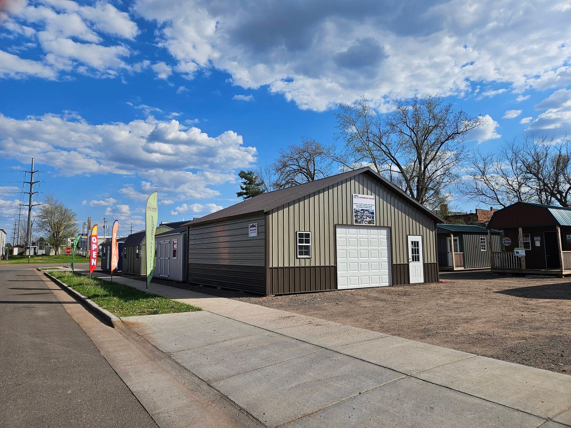 Small roadside building with a white garage door, colorful flags, and a partly cloudy blue sky.