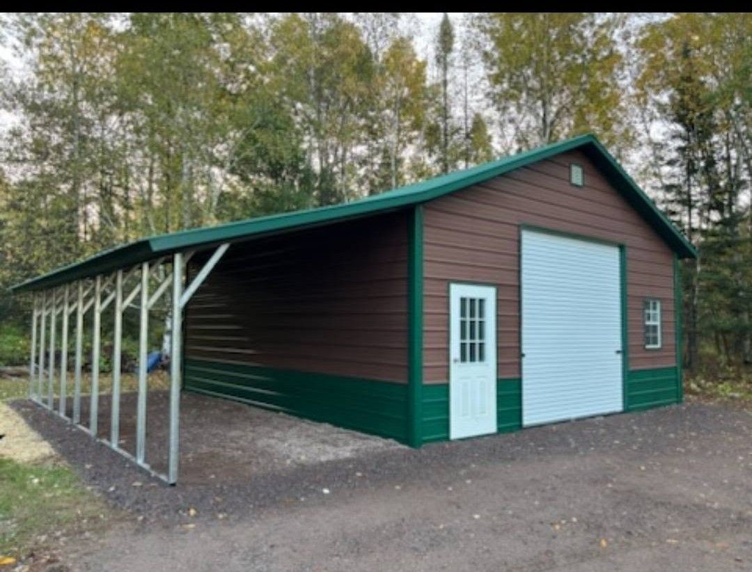 Brown and green metal barn with white roll-up door and attached open-sided shed in a wooded area