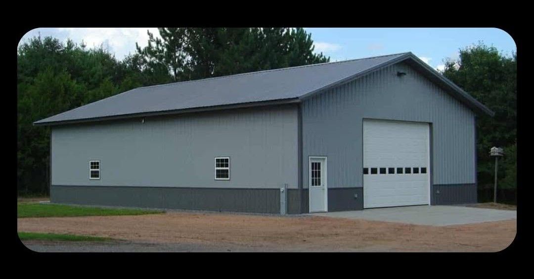 Gray metal garage or workshop building with a white roll-up door and small windows, surrounded by trees