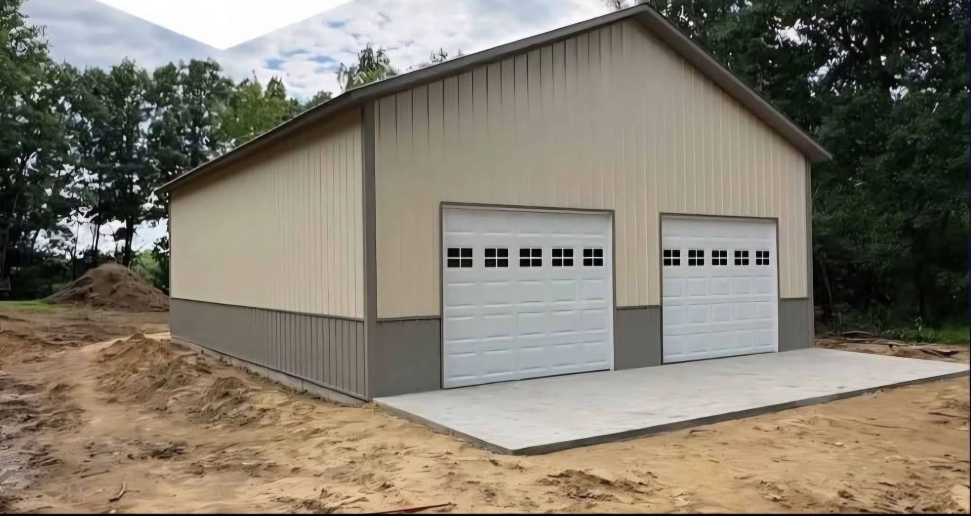 New tan metal garage with two white doors on a concrete slab beside a dirt lot