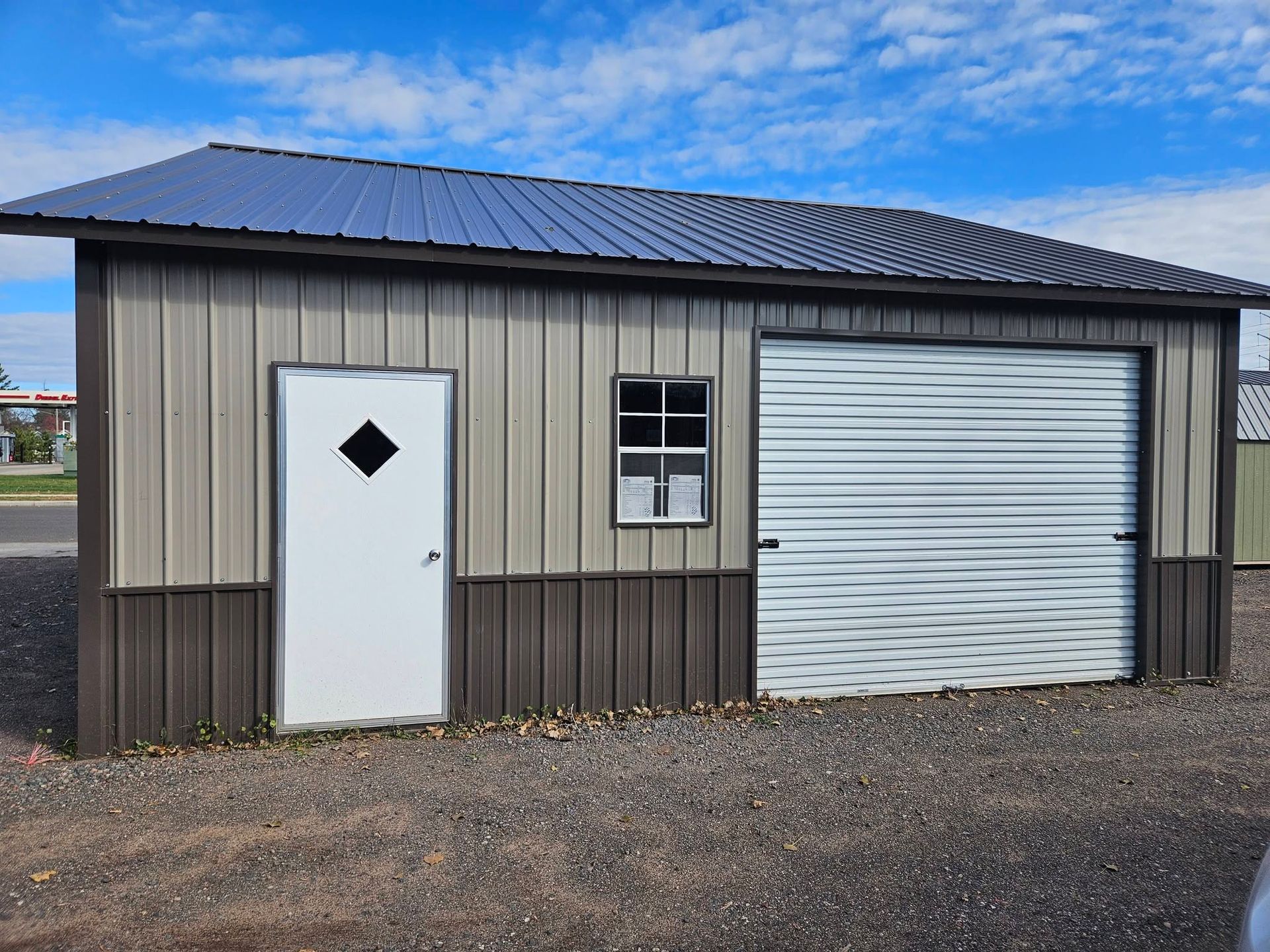 Small beige-and-brown shed with white door, window, and roll-up garage door under a blue sky.