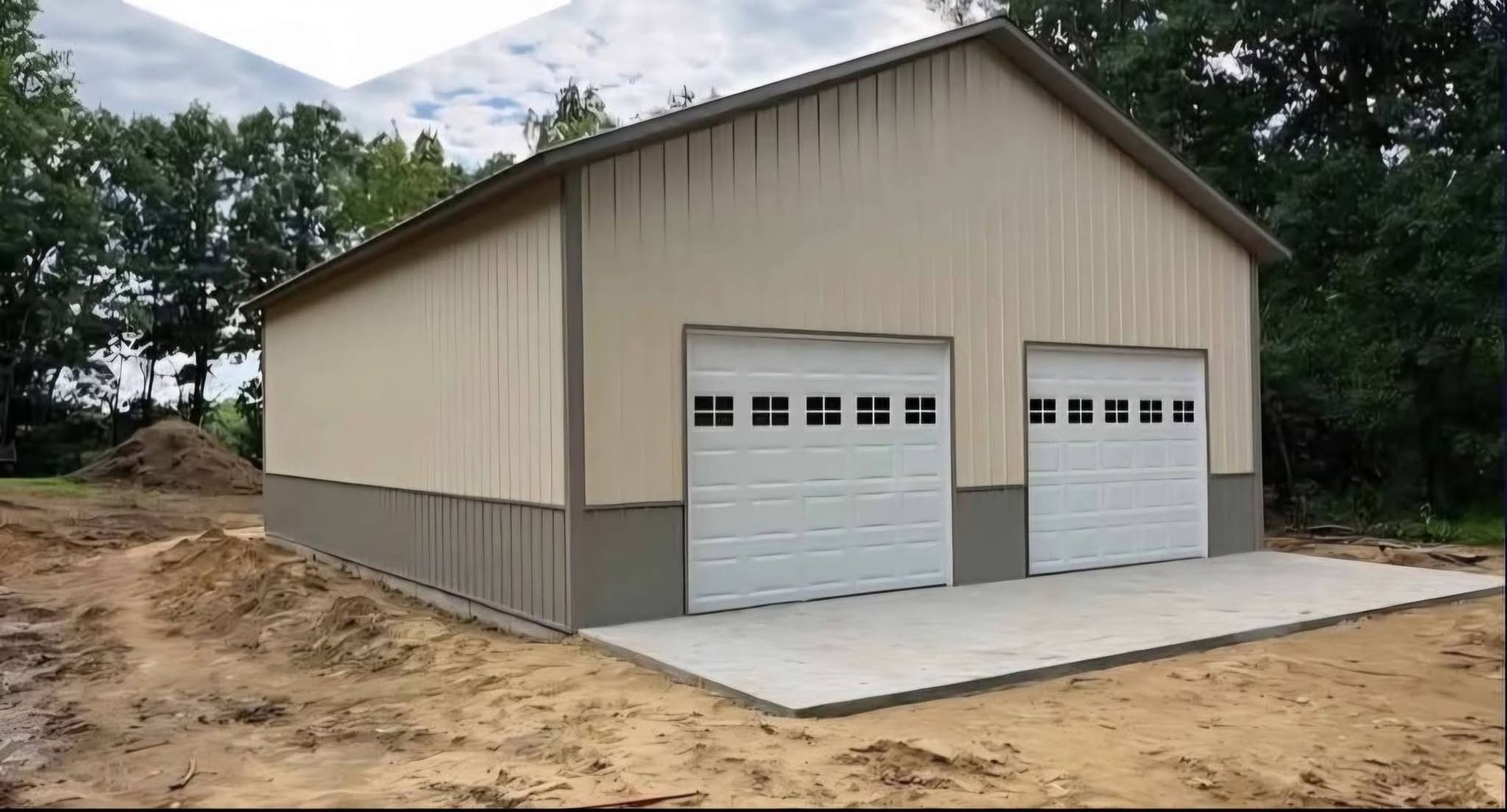 New beige metal garage with two white doors on a concrete pad, set on a dirt lot.
