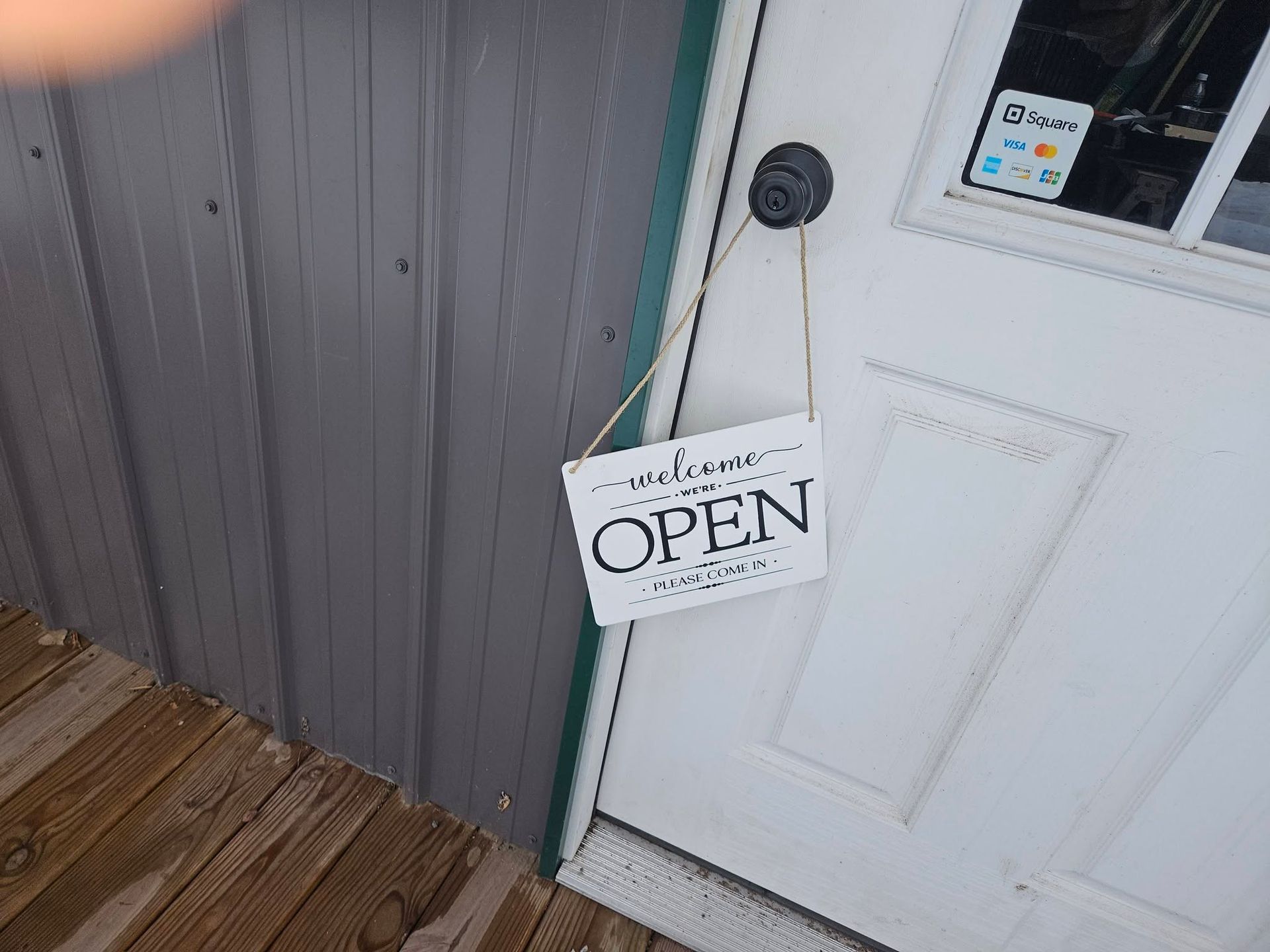 Hanging OPEN sign beside a white door on a gray building wall and wooden porch.