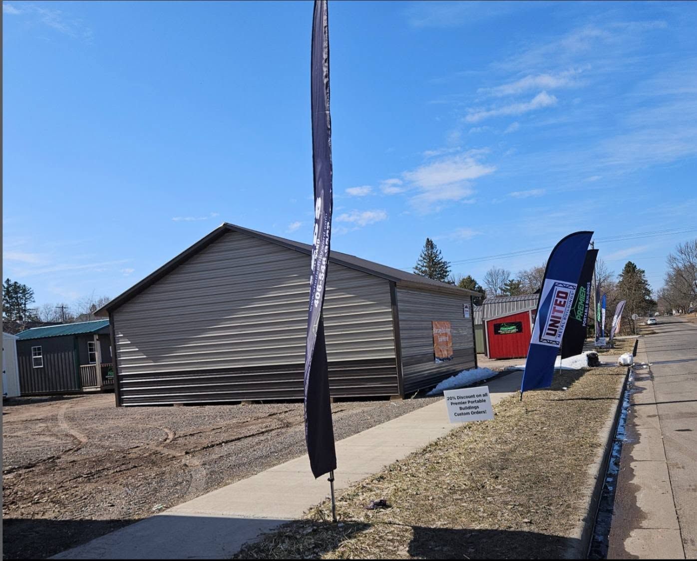 Sidewalk beside a gray building with real estate signs and a red mailbox under a blue sky
