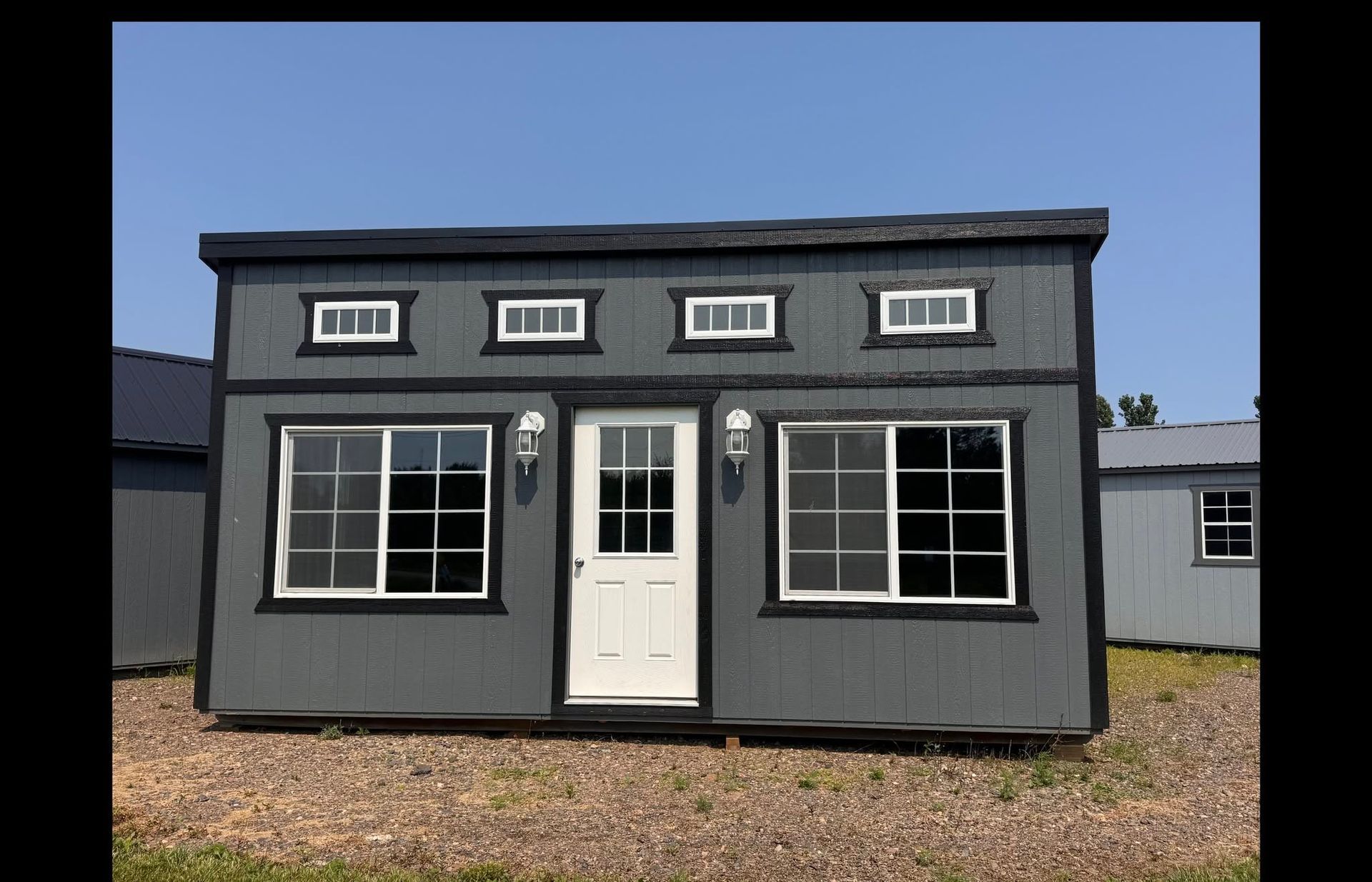 Small gray house façade with white door and windows under a blue sky.