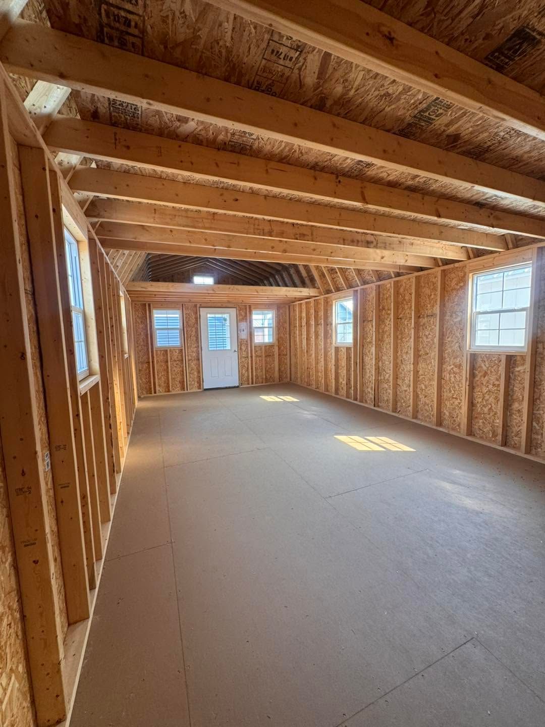 Empty unfinished interior with exposed wooden framing, windows, and a concrete floor