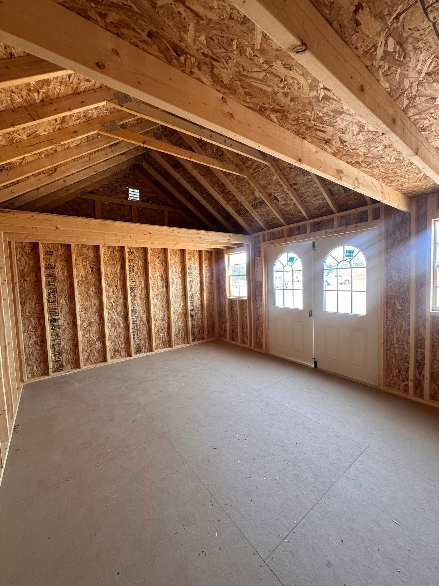 Unfinished attic room with exposed wood framing, insulation, and three arched windows.
