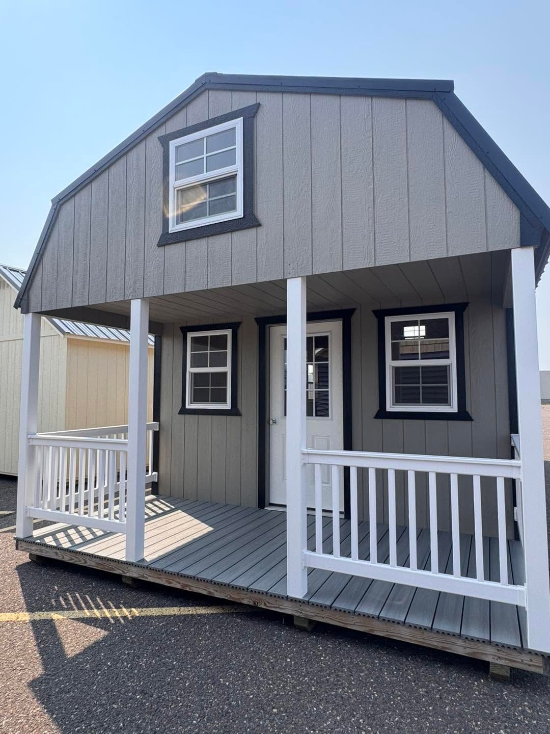 Small gray house with white porch railing and front steps, shown on a paved lot