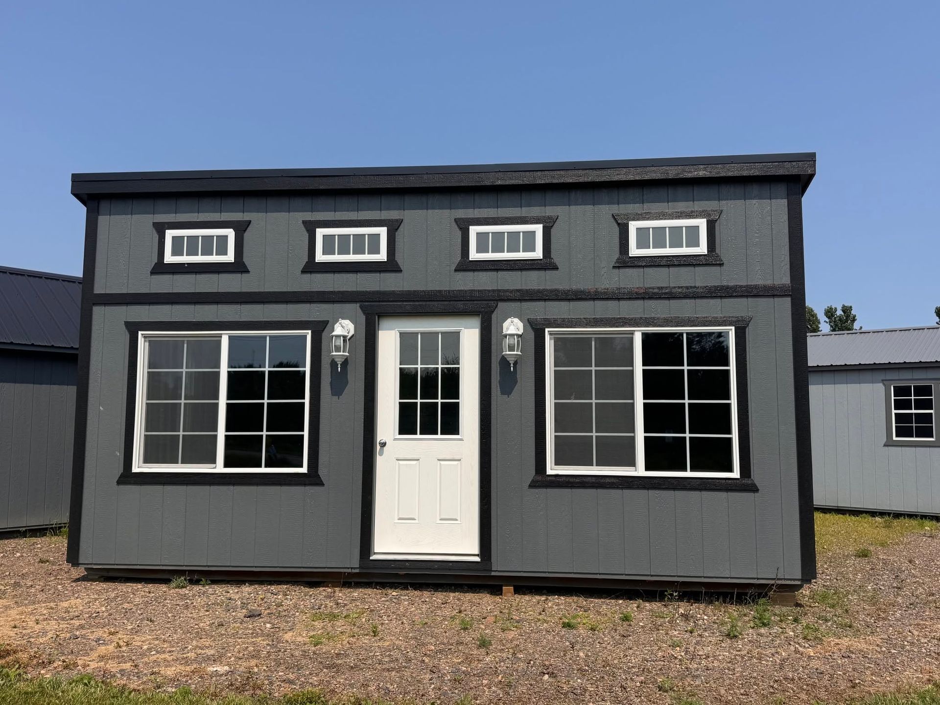 Small gray house with white trim, central door, and large windows on a gravel lot.