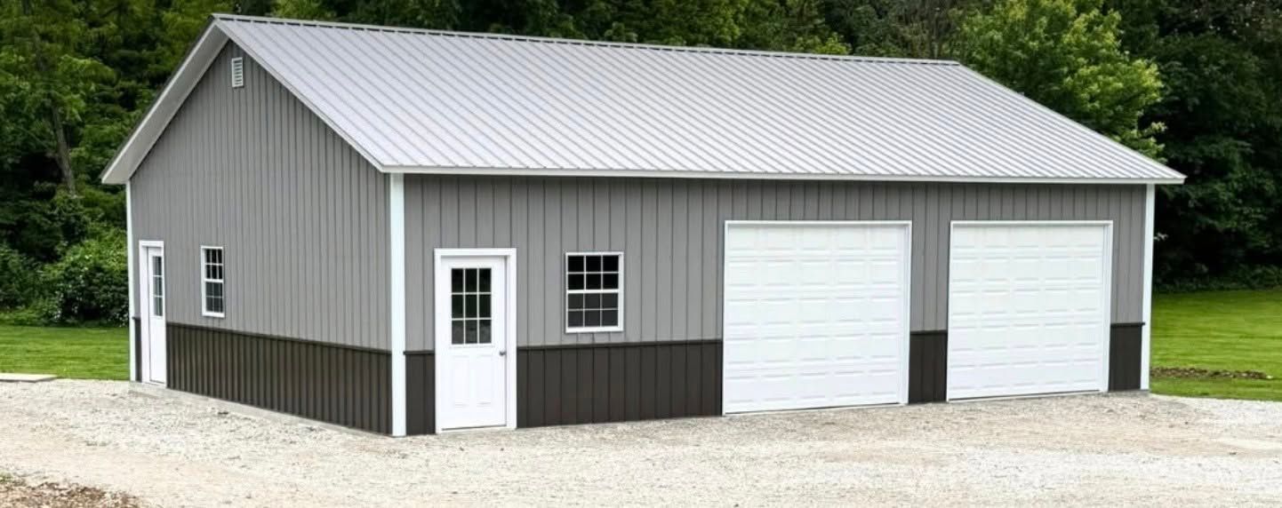 Gray metal garage with white doors and a small side entrance on a gravel lot