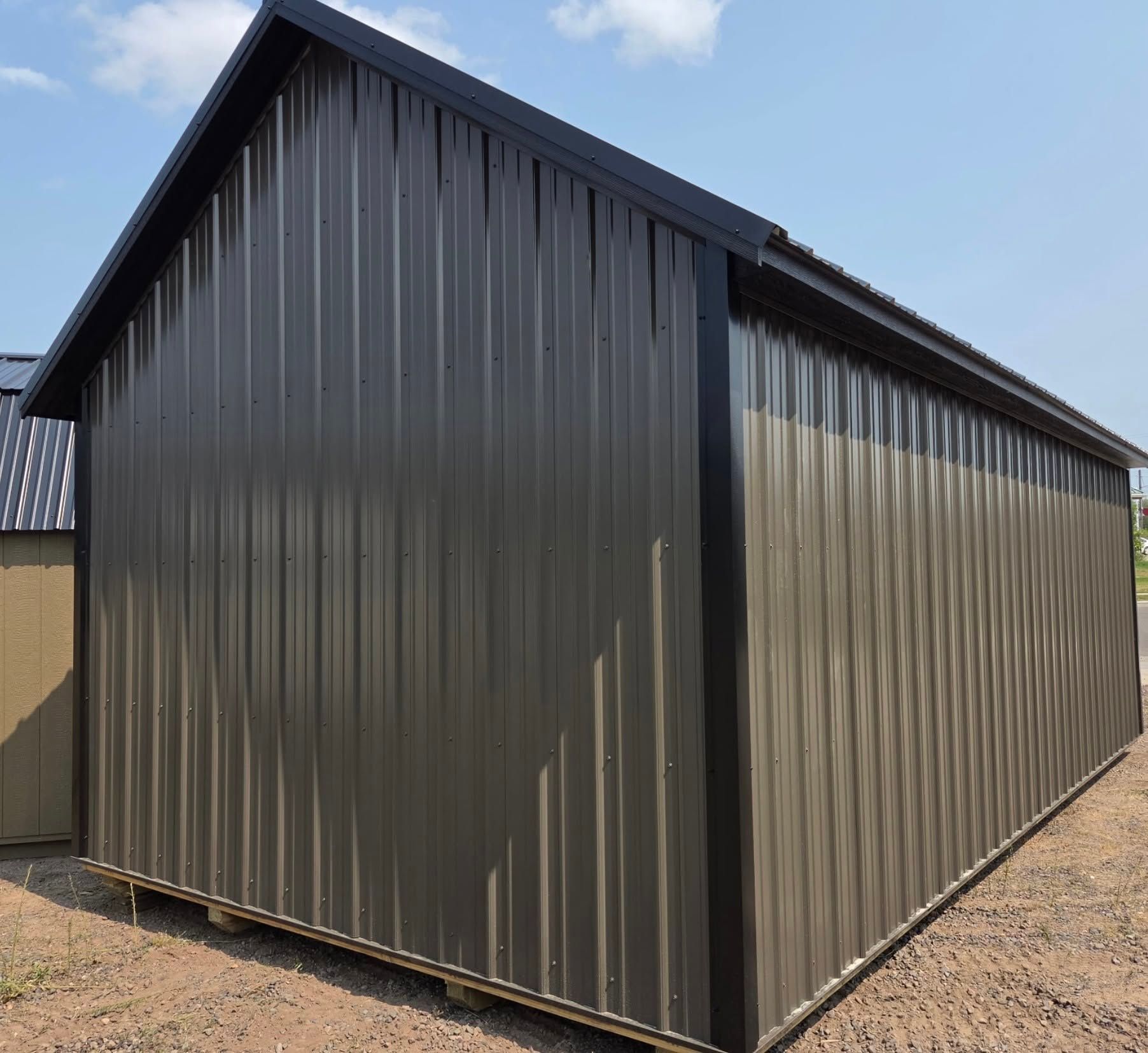 Dark gray metal storage shed with a gabled roof on a gravel lot