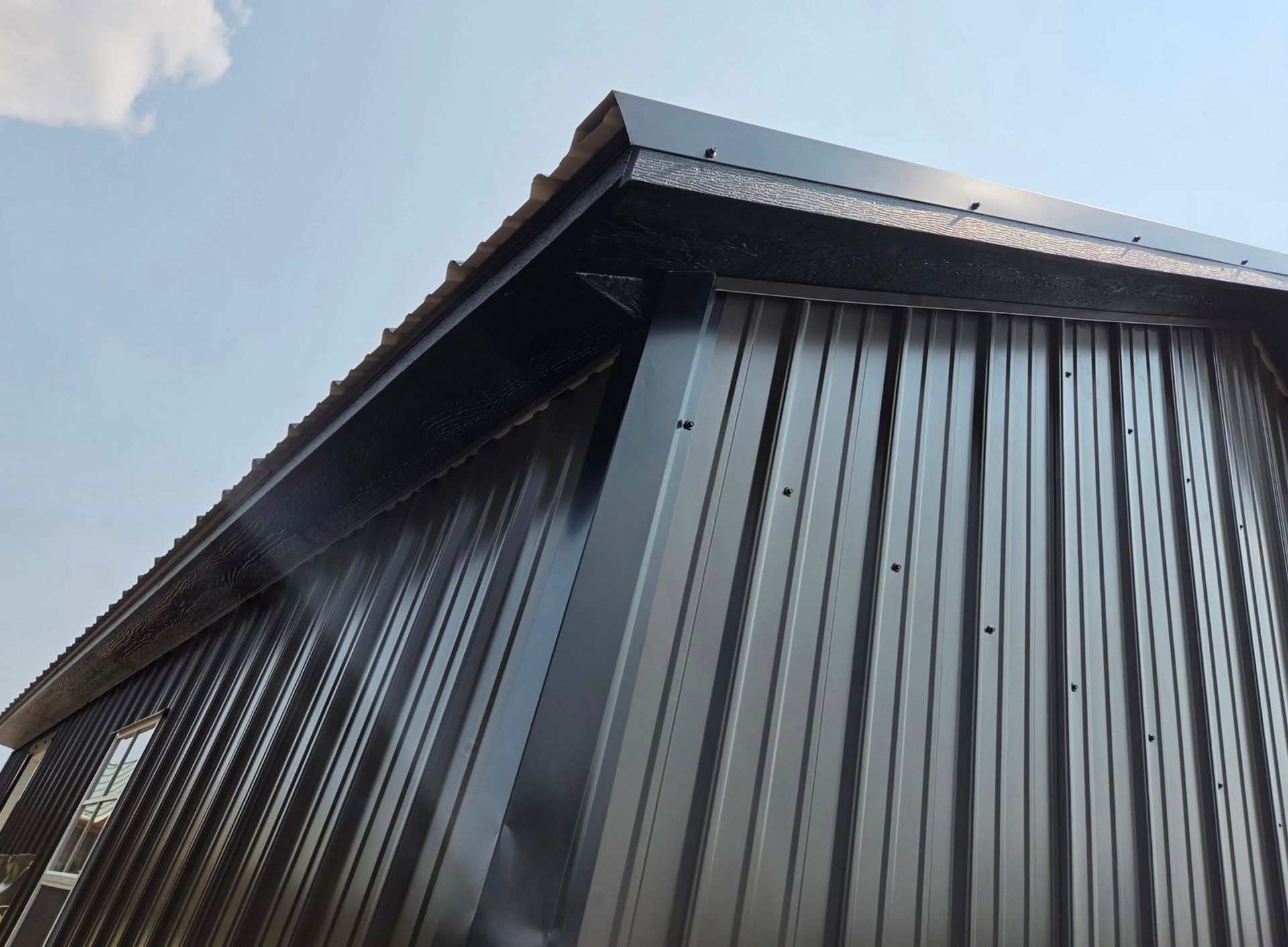 Dark corrugated metal building exterior with a sloped roof against a blue sky