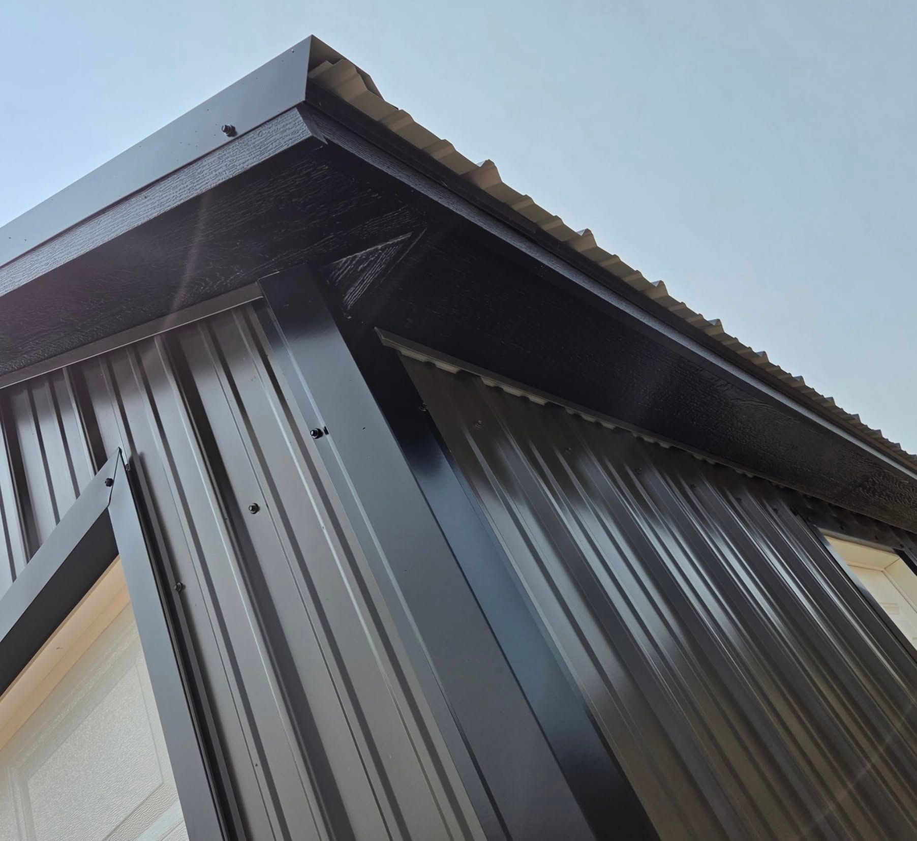 Close-up of a dark metal building corner with ribbed siding and a sloped roof against the sky