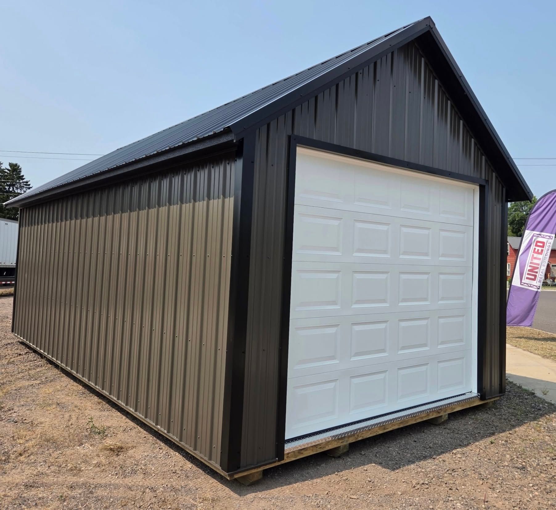 Black metal shed with a white garage door on a gravel lot under a clear sky