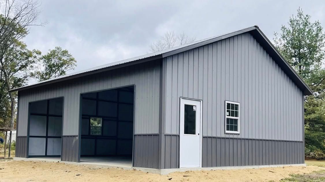 Gray metal barn-style building with large open bay doors and white trim on a sandy lot