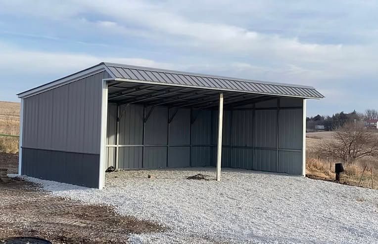 Gray metal shed with open front on a gravel lot under a cloudy sky