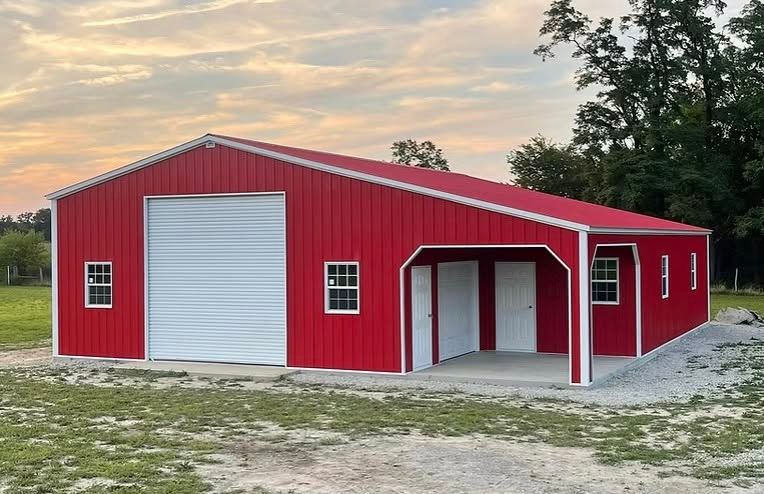 Red metal barn with white doors and trim on a gravel lot at sunset