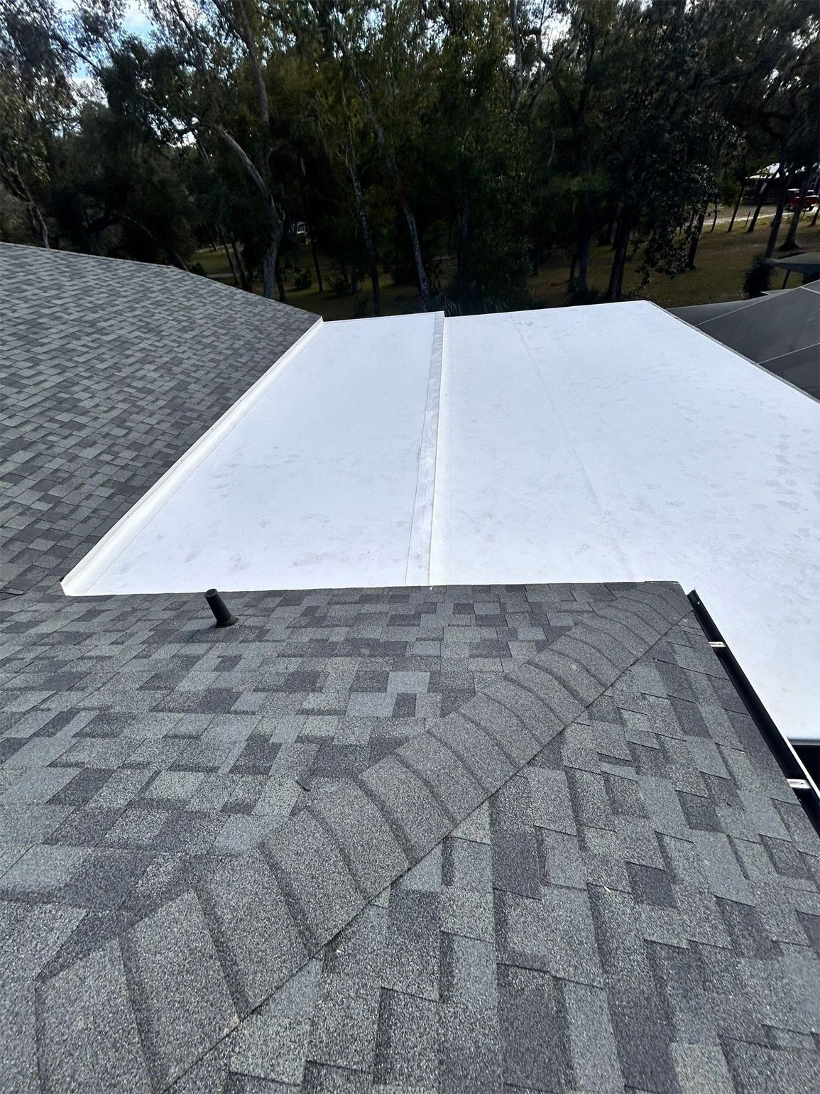 View of a flat roof with gray shingles and a white flat section.