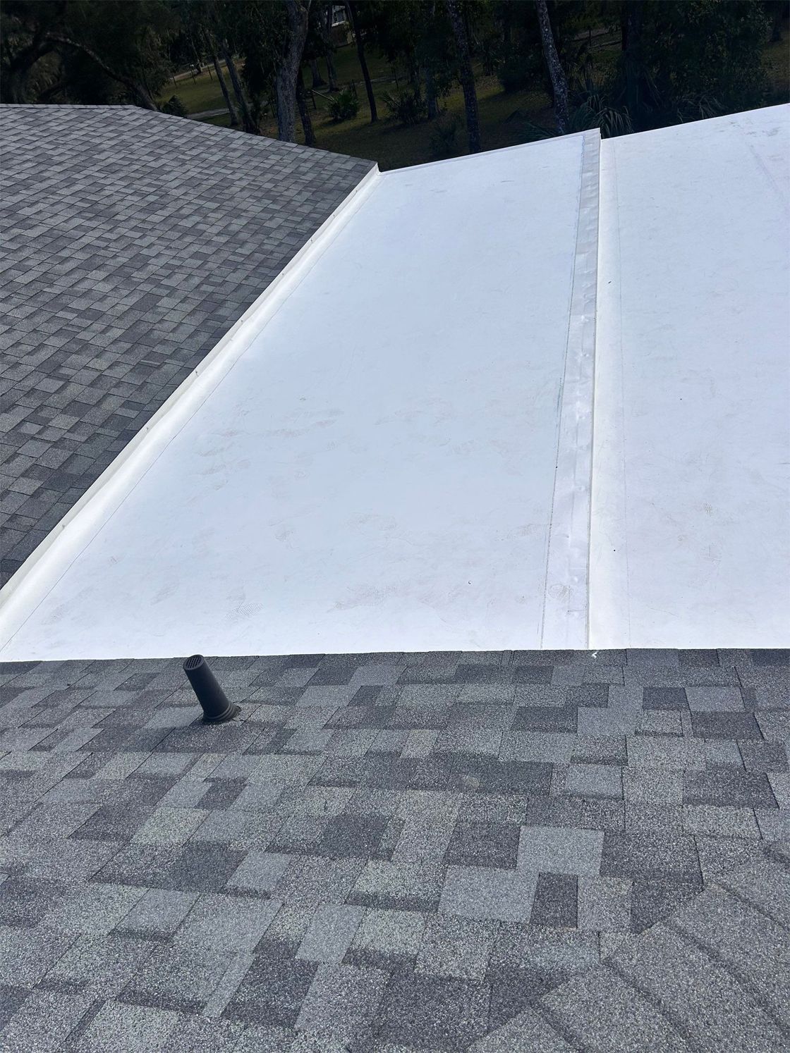 Flat roof with gray shingles next to a white flat roof section.
