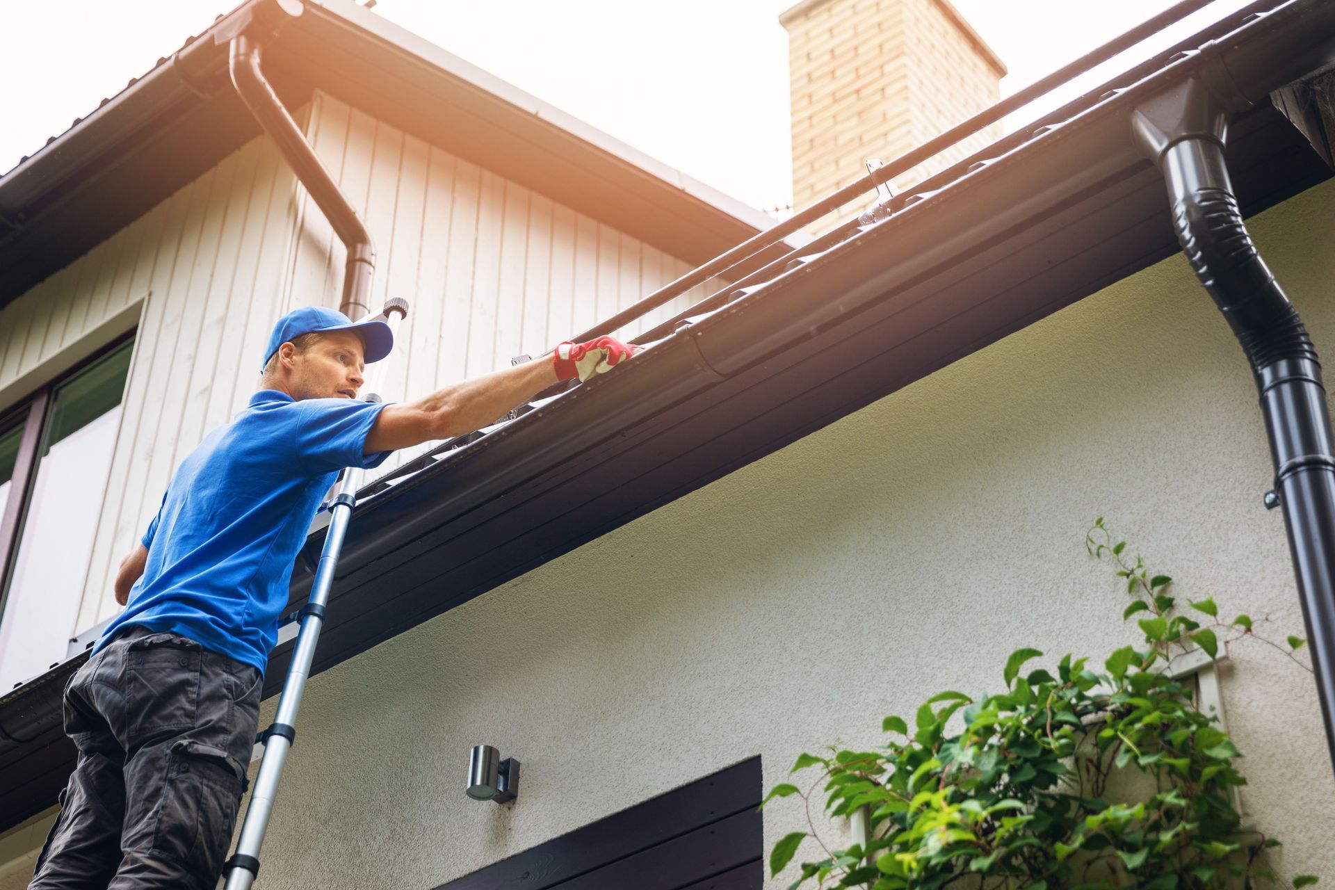 Man on ladder cleaning gutters of a house.