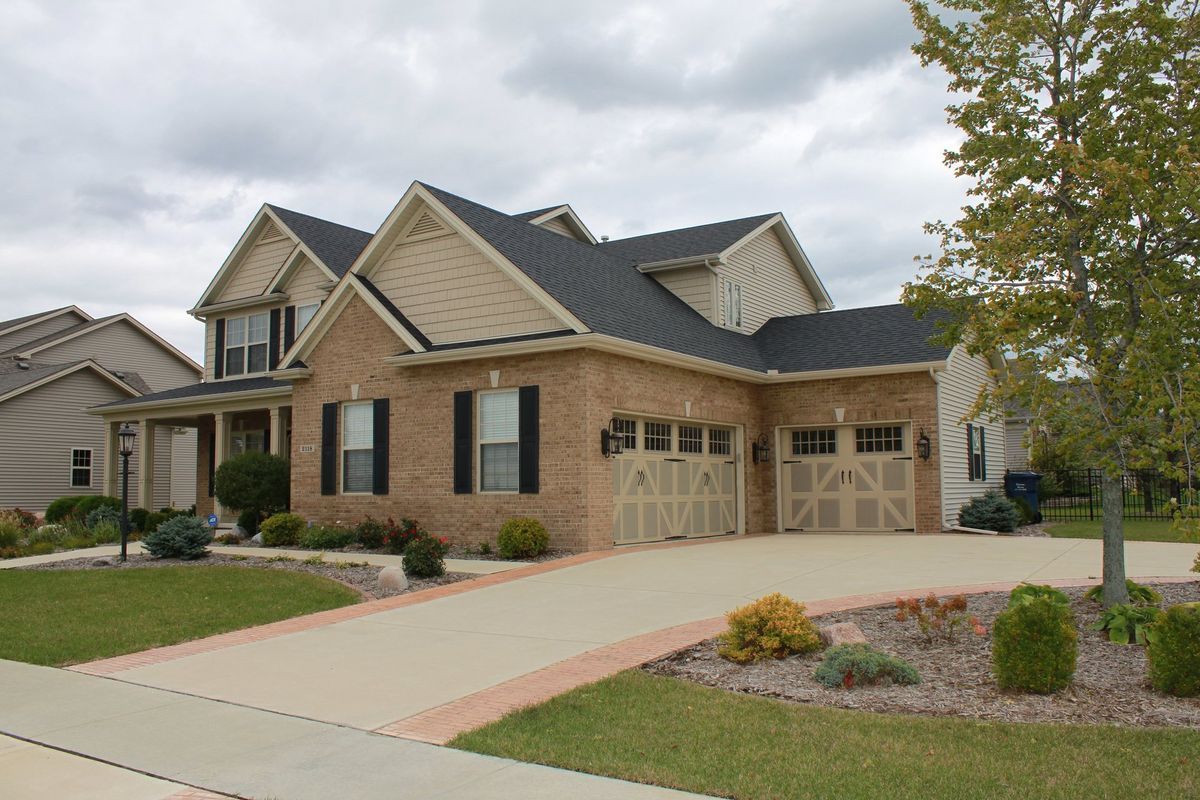 Brick house with two-car garage, driveway, and lawn under a cloudy sky.