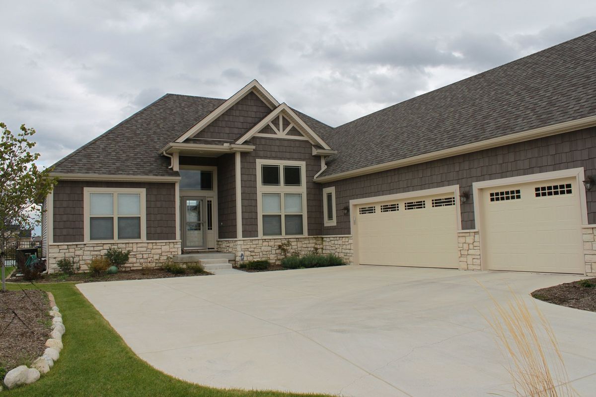 Suburban home with brown siding, light tan garage doors, and a concrete driveway.