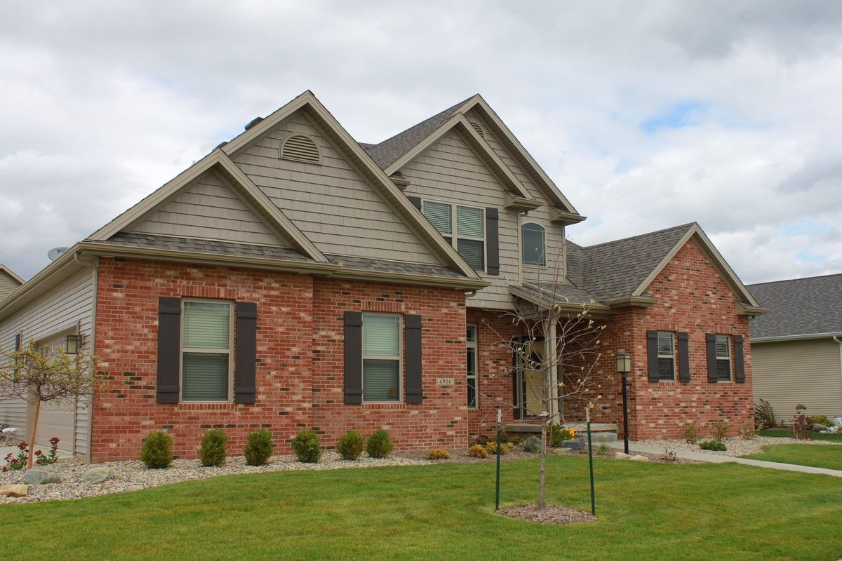 Two-story brick house with brown shutters and roof against a cloudy sky.