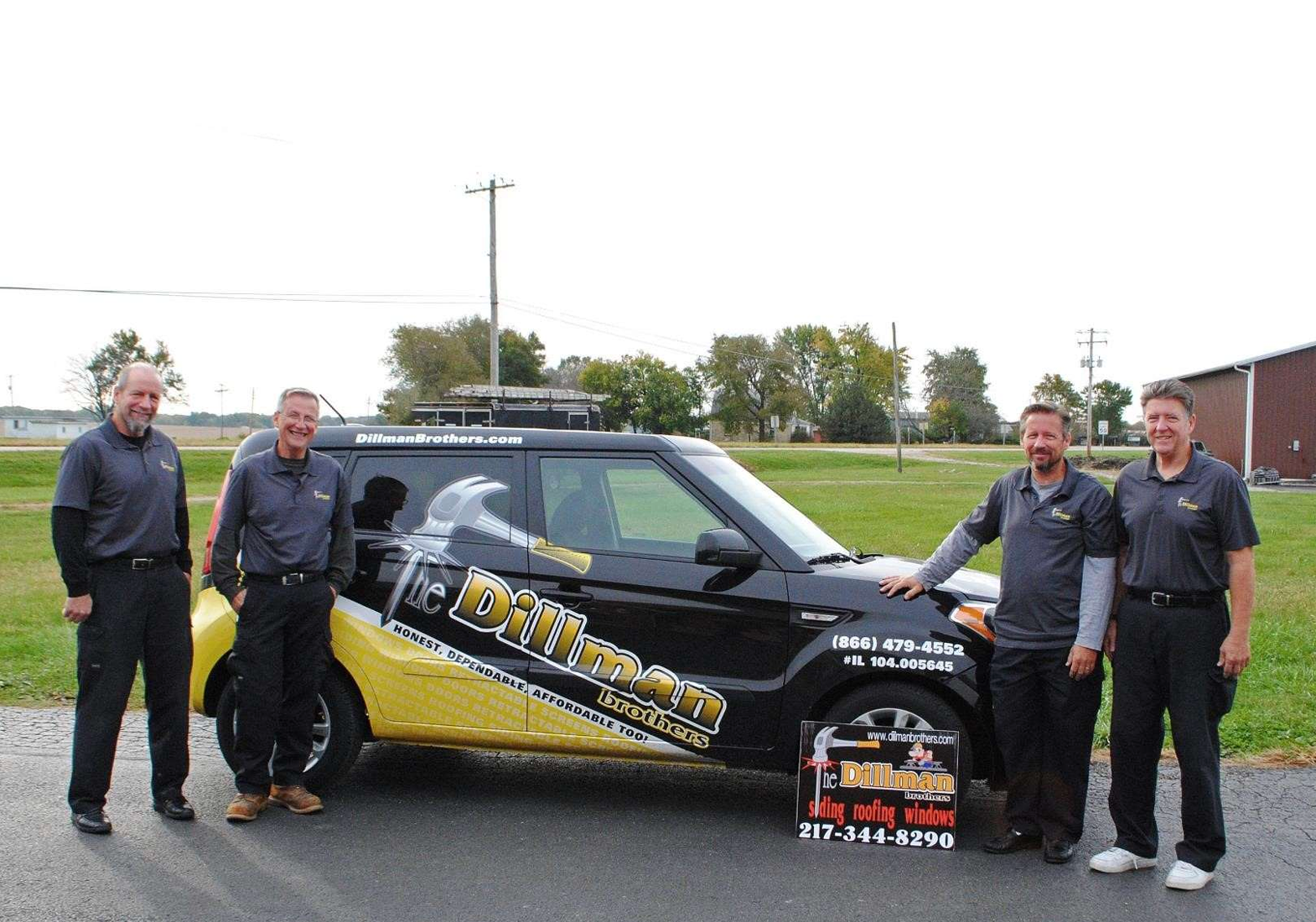 Four men stand beside a car with company branding in a rural setting. The car is black and yellow.