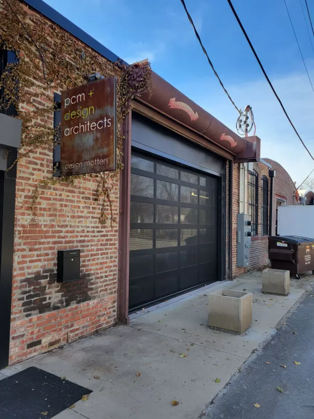 Brick building with a closed garage door and a rusted metal sign that reads "zen! design studio".