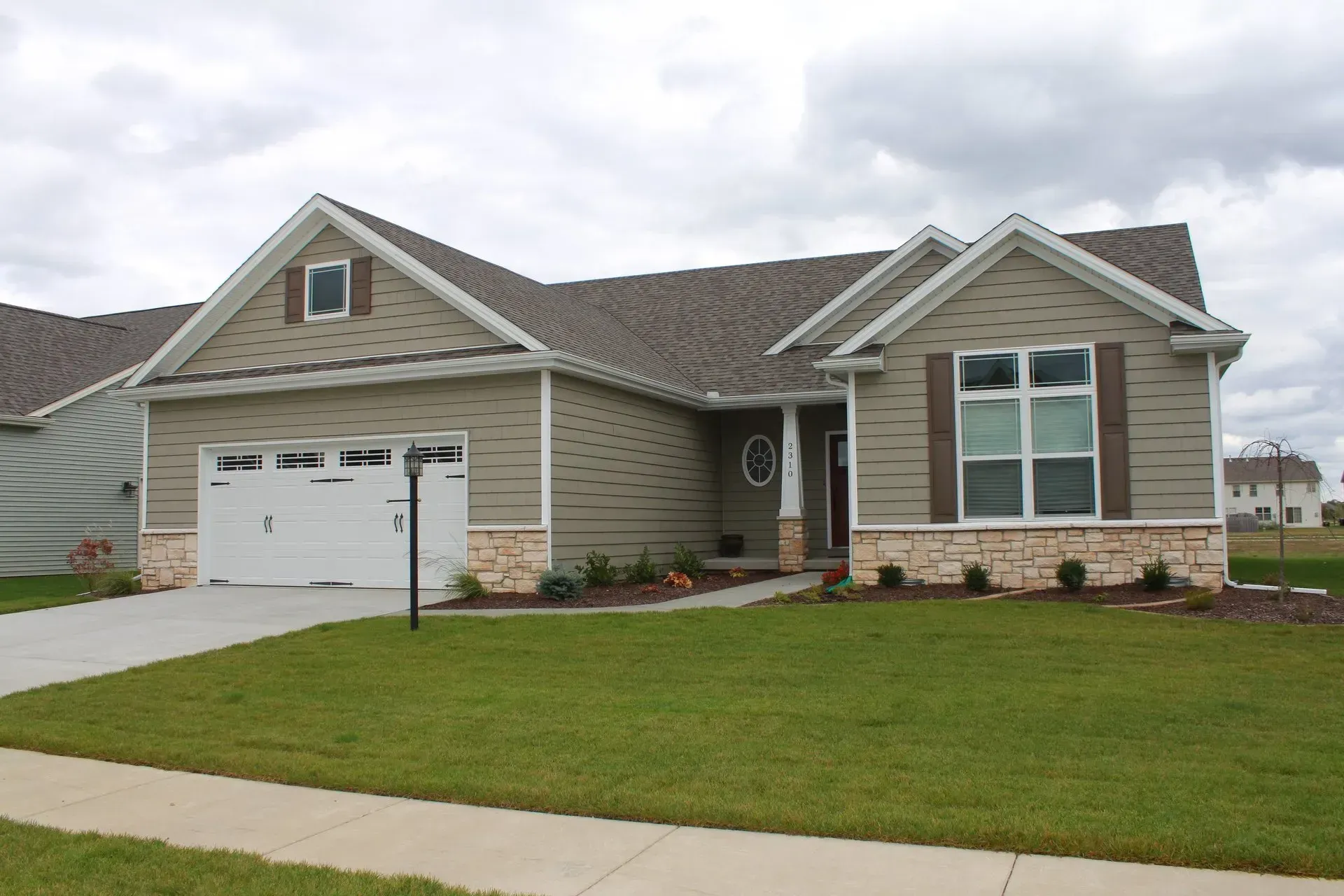 Tan house with white garage door, brown shutters, and stone accents.