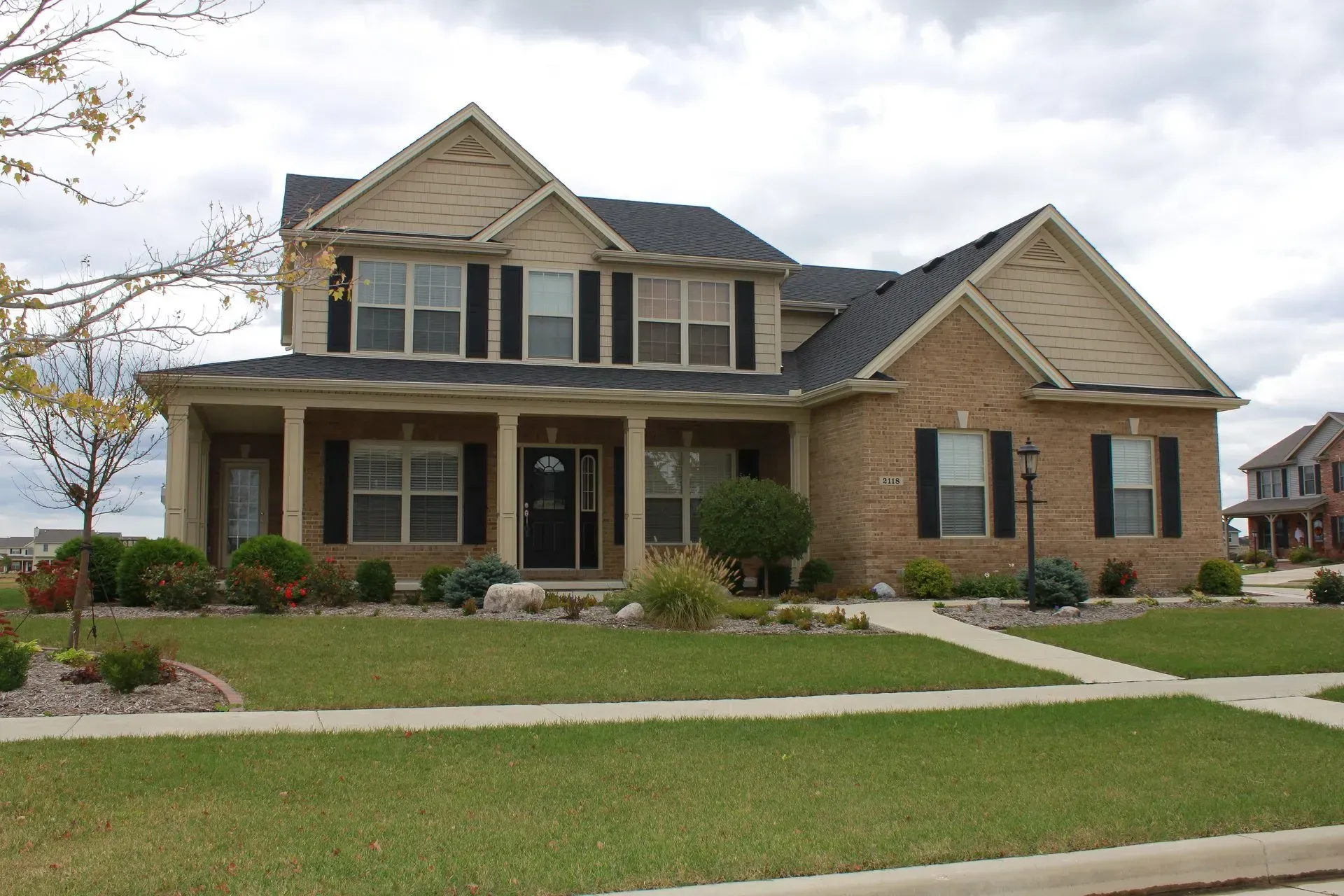 Two-story brick house with a front porch, lawn, and landscaping under a cloudy sky.