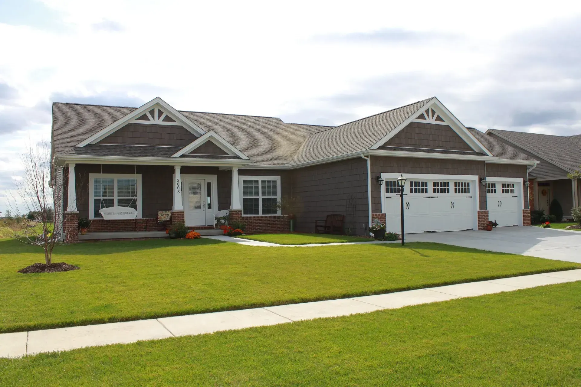 Brown house with white trim, a green lawn, and a sidewalk.