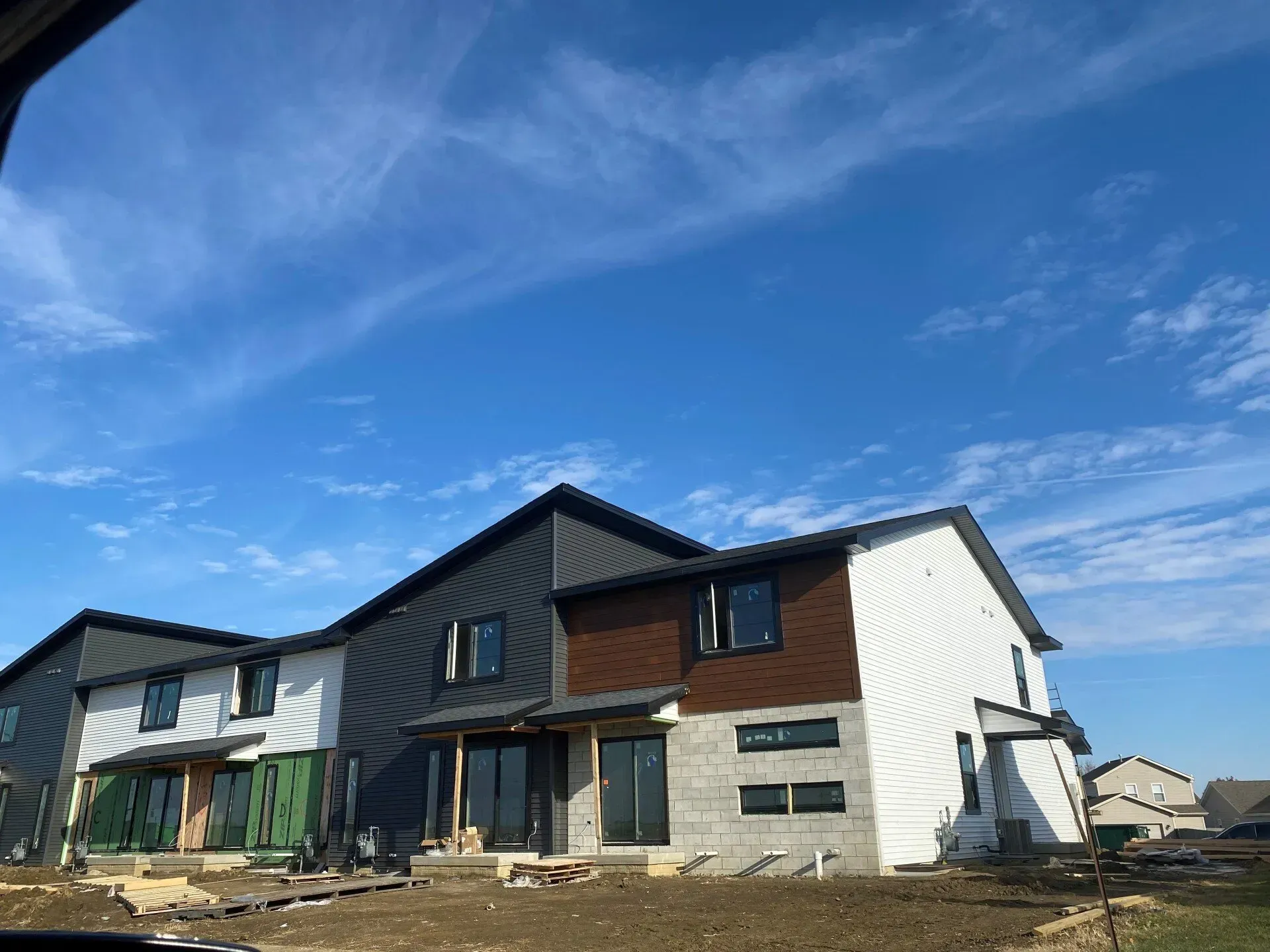 New construction multi-unit homes under a bright blue sky. Exterior finishes include varied siding and stone.