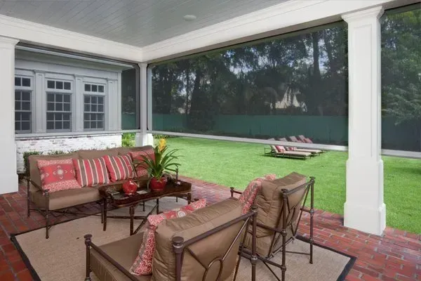 Screened porch with outdoor seating overlooking a backyard. Brown furniture, red brick floor, and green lawn.