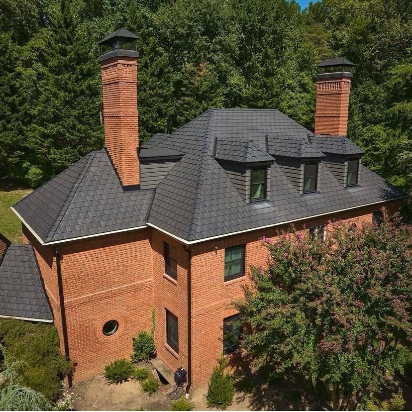 An aerial view of a large brick house with a black roof