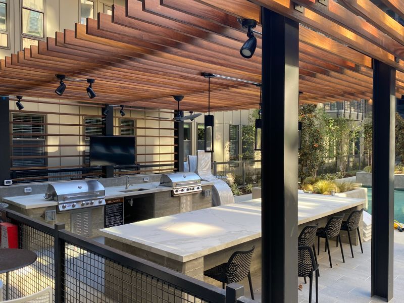 A large outdoor kitchen with a table and chairs under a pergola.