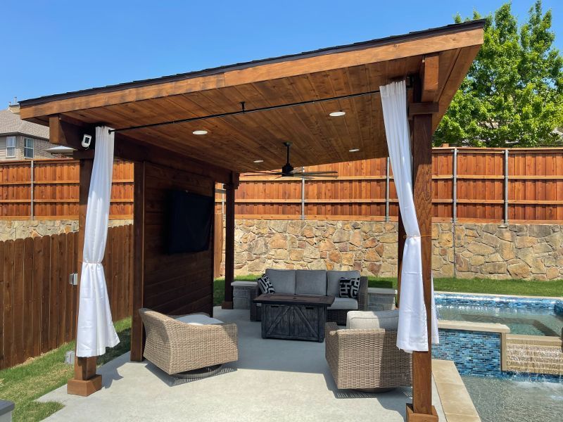 A wooden gazebo with a couch , chairs , table and television.