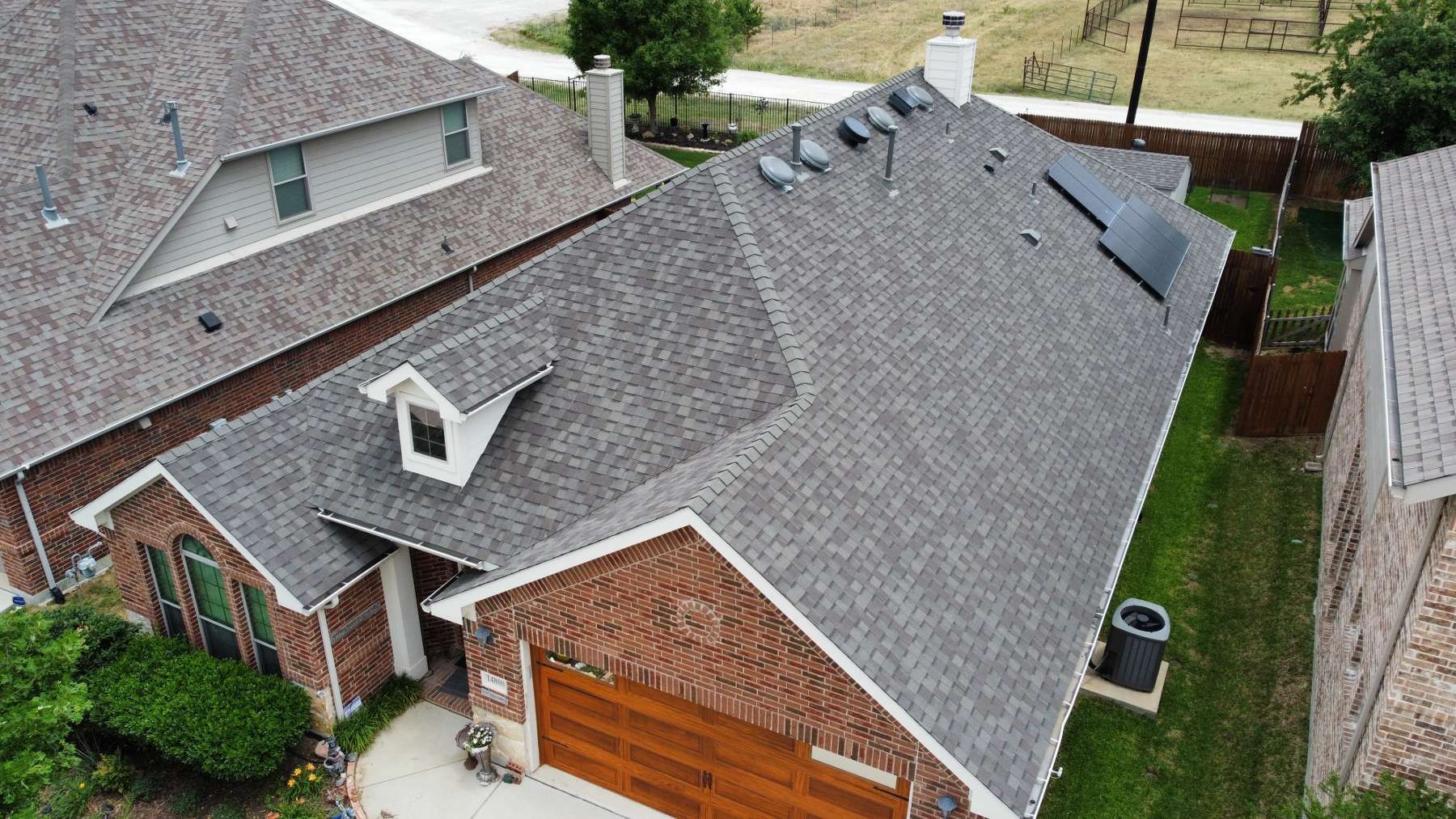 An aerial view of a brick house with a gray roof and a wooden garage door.