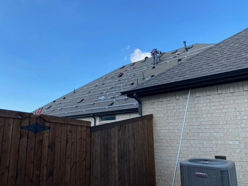 A man is working on the roof of a house next to a wooden fence.