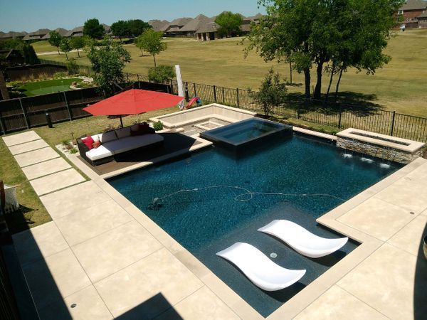 A large swimming pool with two lounge chairs and an umbrella