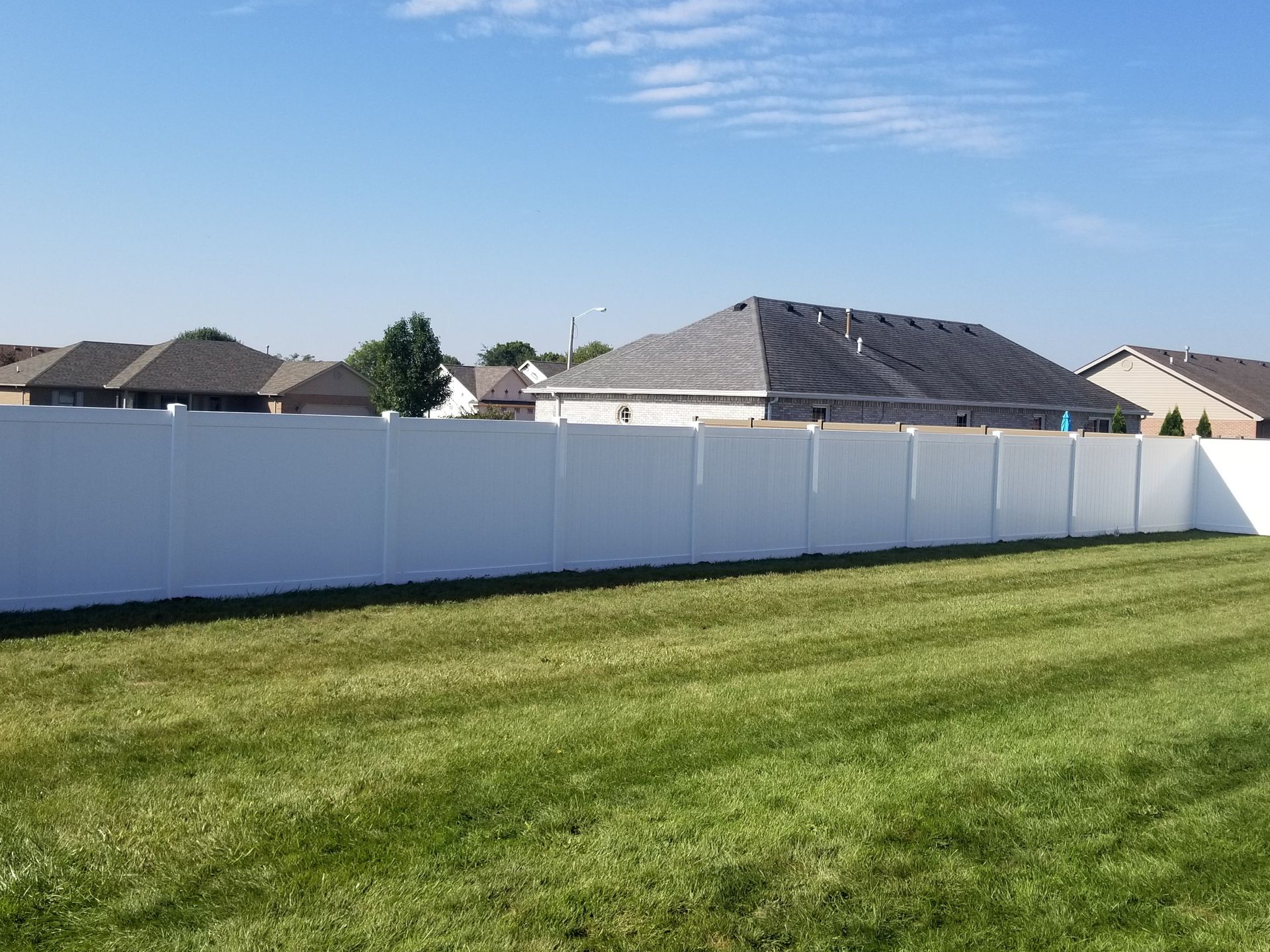 Backyard with green lawn, white fence, and suburban houses under a blue sky