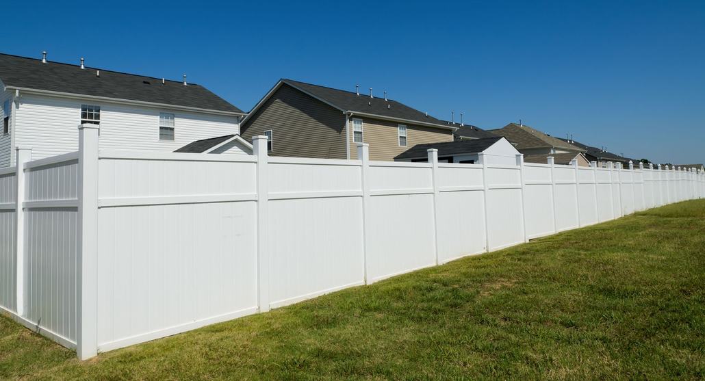 White vinyl privacy fence along suburban houses beside a grassy lawn under a clear blue sky