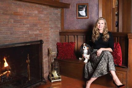 Woman sitting on a wooden bench with a dog beside a brick fireplace in a cozy room