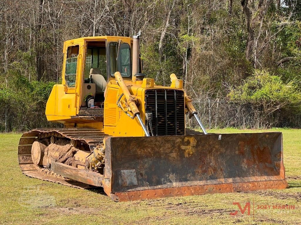 Yellow bulldozer with front blade, tracks, and a cab, parked on grass.
