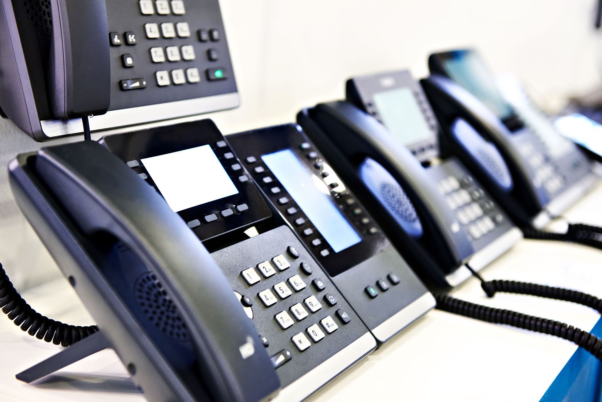 A row of black office desk phones arranged in a line on a white surface, receding into the background.