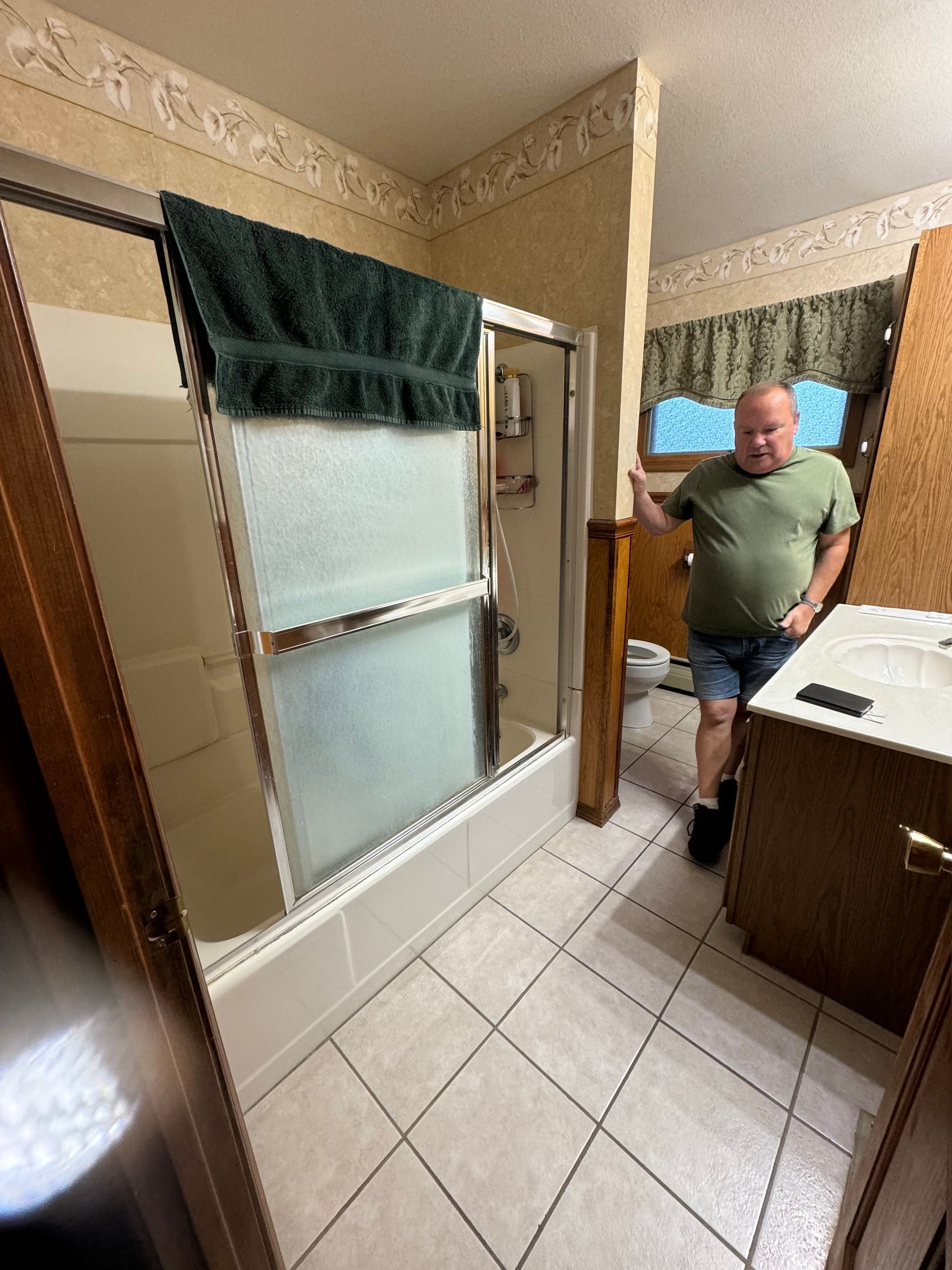 A man is standing in a bathroom next to a shower