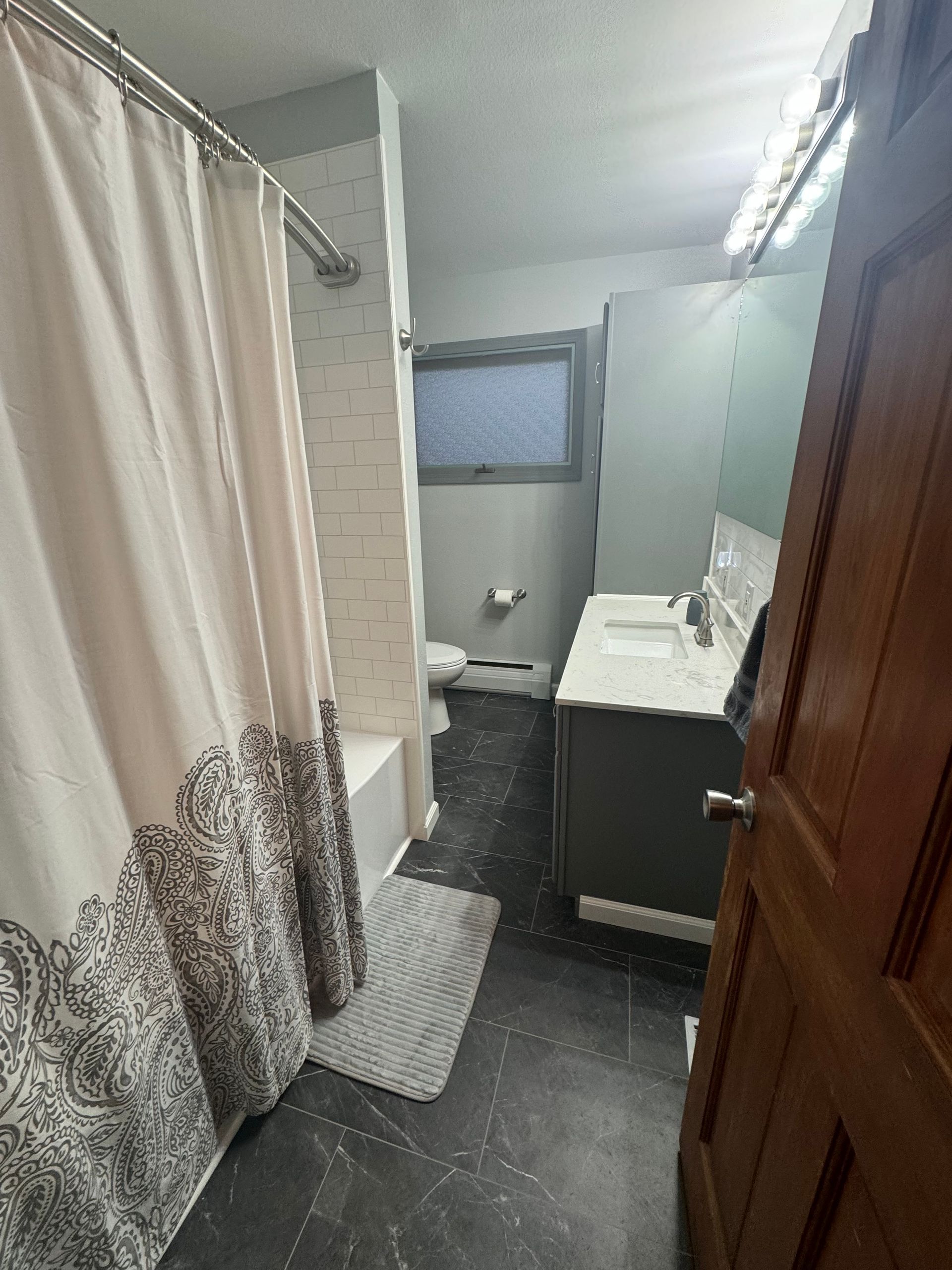 A bathroom with a shower curtain, sink, toilet and mirror